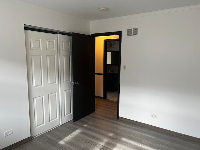 unfurnished bedroom with crown molding, a closet, and wood-type flooring