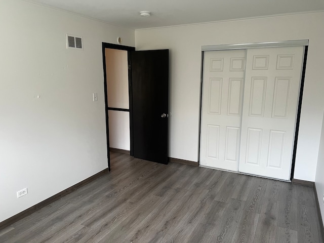 unfurnished bedroom featuring dark hardwood / wood-style flooring, ornamental molding, and a closet