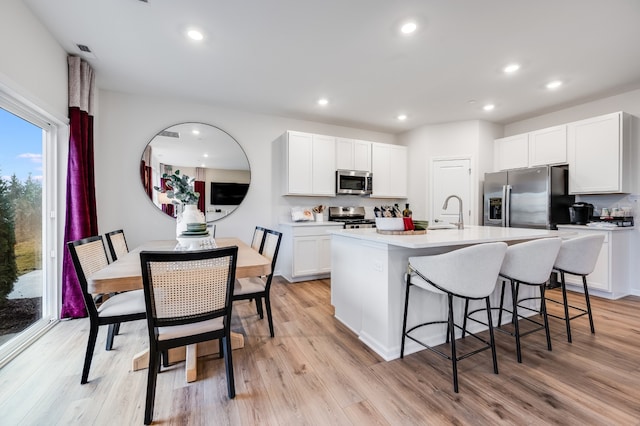 kitchen featuring white cabinets, light hardwood / wood-style floors, an island with sink, a breakfast bar, and appliances with stainless steel finishes