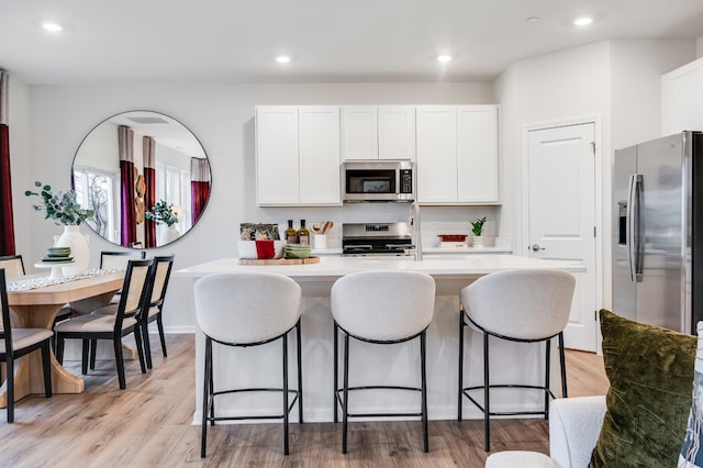 kitchen with appliances with stainless steel finishes, light hardwood / wood-style flooring, white cabinets, and an island with sink