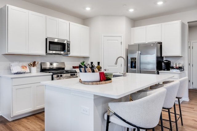 kitchen featuring stainless steel appliances, a center island with sink, white cabinetry, and light wood-type flooring