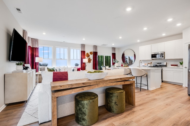 kitchen with stainless steel appliances, light hardwood / wood-style floors, a kitchen breakfast bar, and white cabinetry