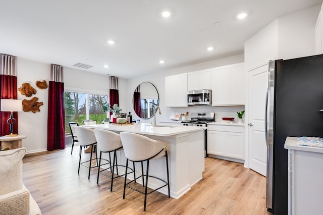 kitchen with a breakfast bar, light wood-type flooring, a kitchen island with sink, white cabinetry, and appliances with stainless steel finishes