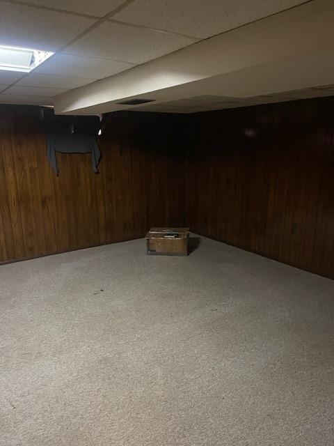 basement featuring carpet flooring, a paneled ceiling, and wooden walls