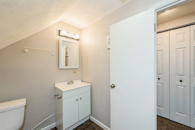 bathroom with a textured ceiling, vanity, lofted ceiling, and toilet