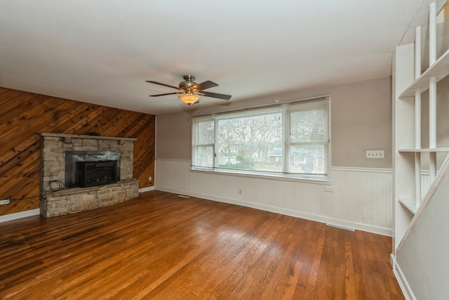 unfurnished living room with wood walls, hardwood / wood-style floors, and ceiling fan