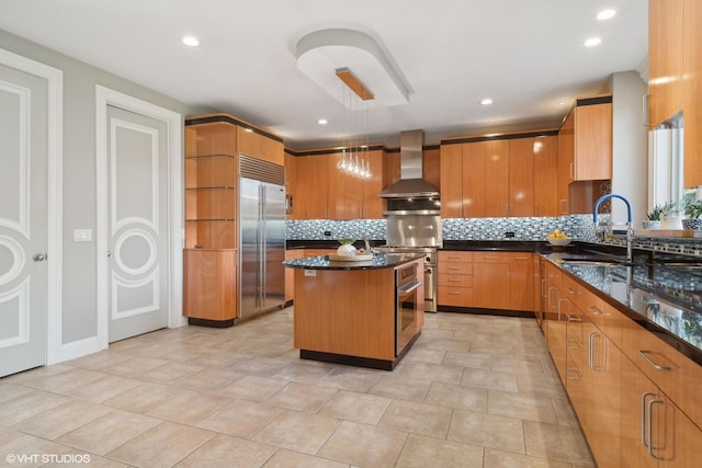 kitchen with decorative backsplash, wall chimney exhaust hood, stainless steel appliances, sink, and a kitchen island