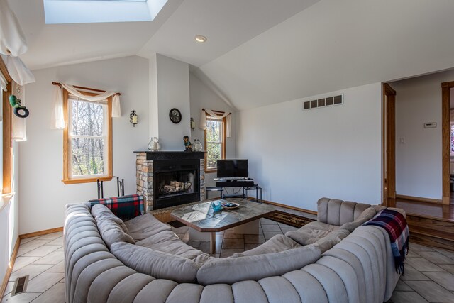 living room with lofted ceiling with skylight, a wealth of natural light, and a stone fireplace