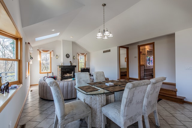 dining area with lofted ceiling with skylight, a fireplace, and an inviting chandelier