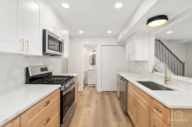 kitchen featuring sink, appliances with stainless steel finishes, light hardwood / wood-style floors, light stone counters, and white cabinetry