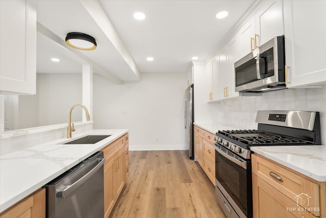 kitchen featuring sink, light stone counters, appliances with stainless steel finishes, white cabinets, and light wood-type flooring