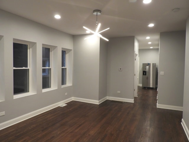 empty room featuring dark wood-type flooring and an inviting chandelier