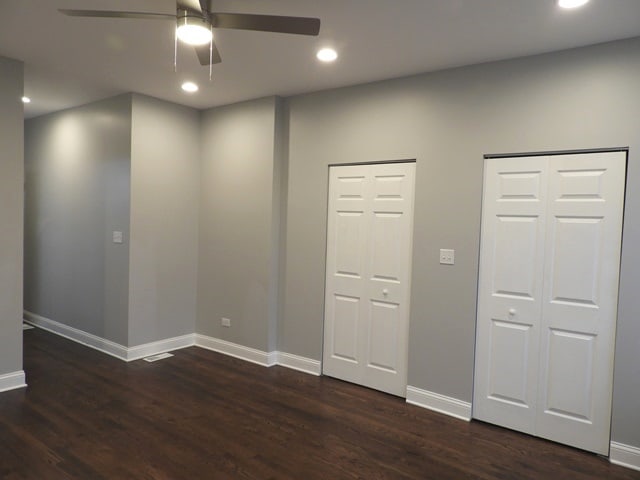 unfurnished bedroom with ceiling fan, dark hardwood / wood-style flooring, and multiple closets