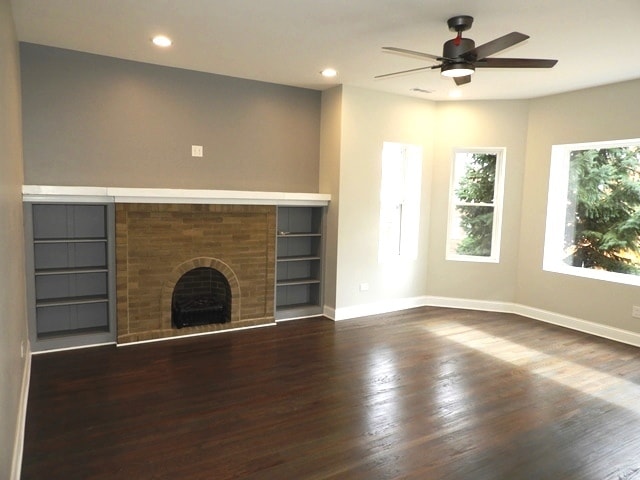 unfurnished living room with ceiling fan, dark hardwood / wood-style flooring, and a brick fireplace