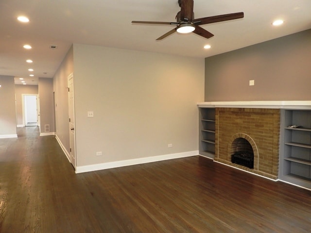 unfurnished living room featuring a brick fireplace, ceiling fan, and dark wood-type flooring