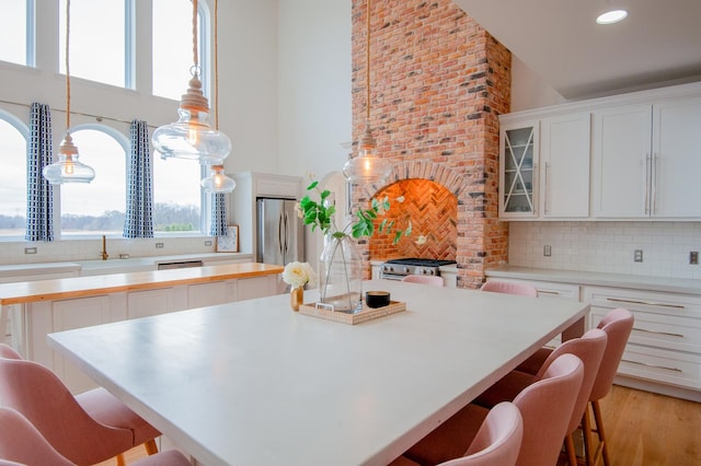 kitchen featuring stainless steel fridge, tasteful backsplash, pendant lighting, light hardwood / wood-style floors, and white cabinetry