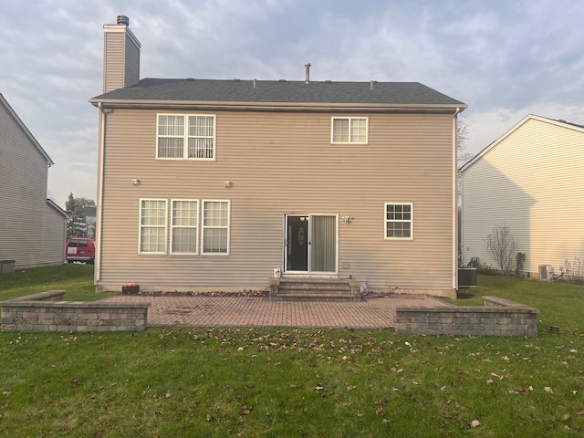 back of property with entry steps, a patio area, central air condition unit, a yard, and a chimney