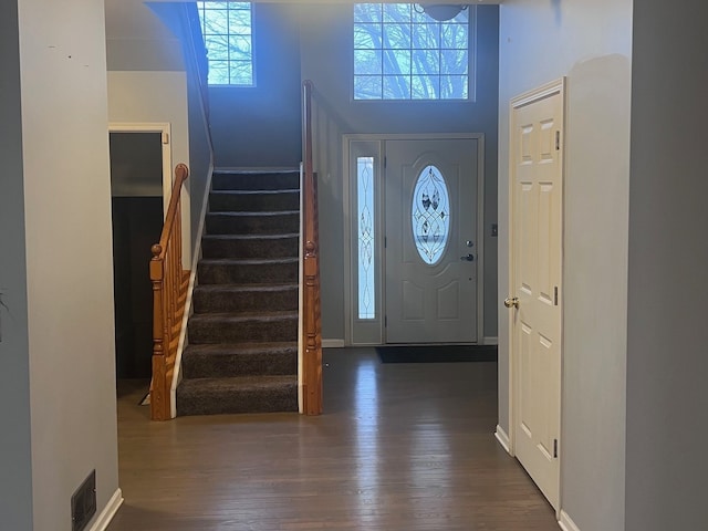 foyer entrance featuring stairway, dark wood-type flooring, healthy amount of natural light, baseboards, and a towering ceiling