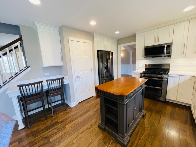 kitchen featuring white cabinetry, stainless steel appliances, dark hardwood / wood-style floors, backsplash, and a kitchen island