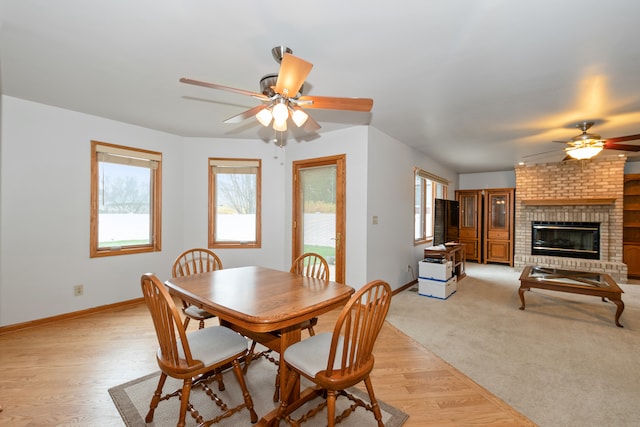 dining area featuring light hardwood / wood-style floors, a brick fireplace, plenty of natural light, and ceiling fan