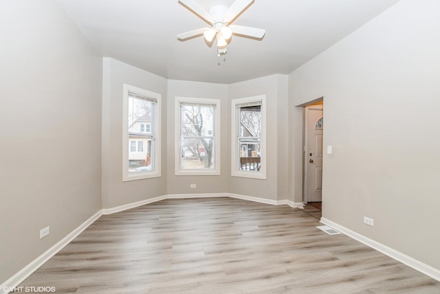 empty room featuring light wood-style flooring, a ceiling fan, a wealth of natural light, and baseboards