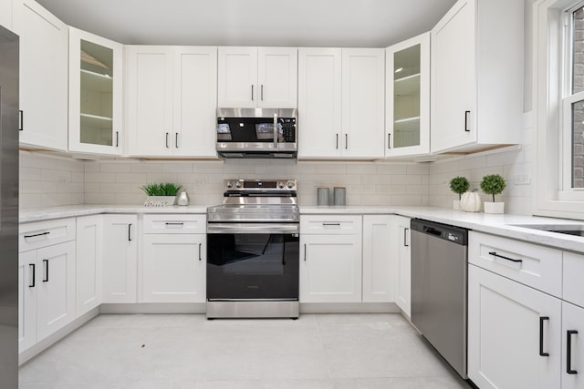 kitchen featuring light stone countertops, white cabinetry, stainless steel appliances, tasteful backsplash, and light tile patterned floors