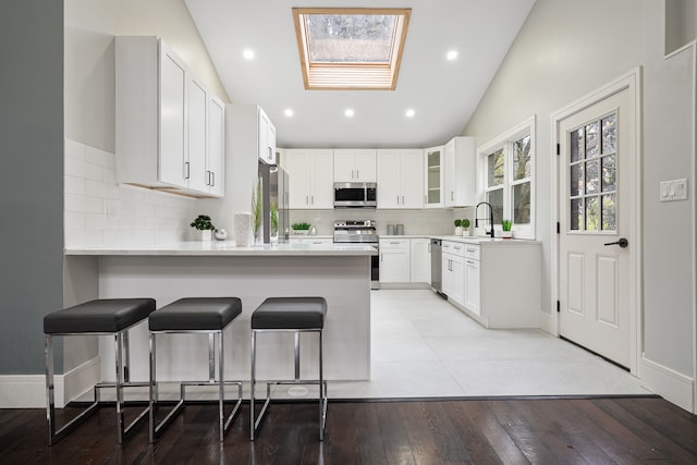 kitchen featuring stainless steel appliances, light hardwood / wood-style flooring, a kitchen bar, vaulted ceiling with skylight, and white cabinets