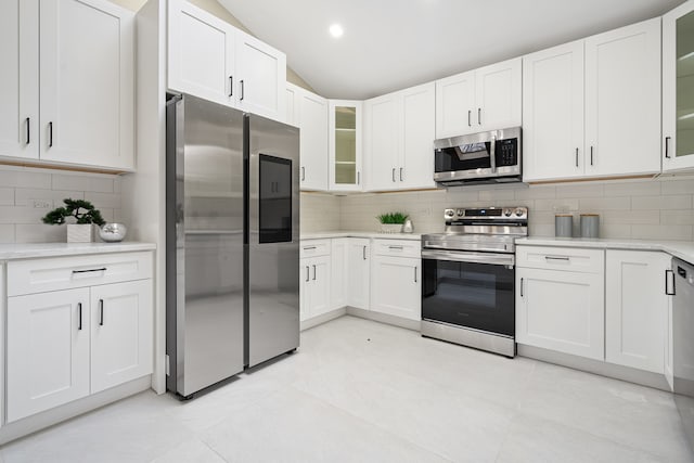 kitchen featuring decorative backsplash, appliances with stainless steel finishes, vaulted ceiling, light tile patterned floors, and white cabinetry