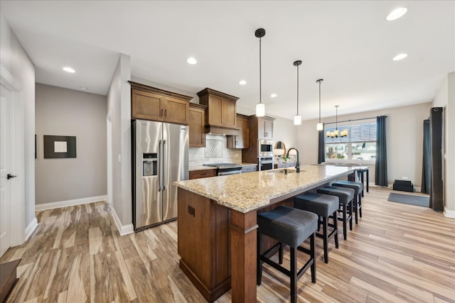 kitchen with a kitchen bar, light wood-type flooring, stainless steel appliances, a large island with sink, and decorative light fixtures