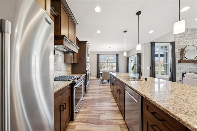 kitchen with sink, hanging light fixtures, light hardwood / wood-style flooring, appliances with stainless steel finishes, and light stone counters