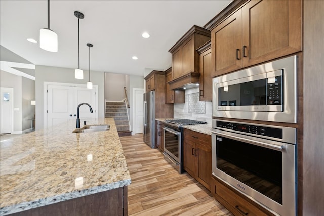 kitchen featuring appliances with stainless steel finishes, light stone counters, sink, pendant lighting, and light hardwood / wood-style floors