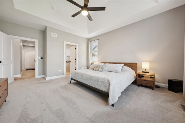 bedroom with ceiling fan, light colored carpet, and ensuite bath