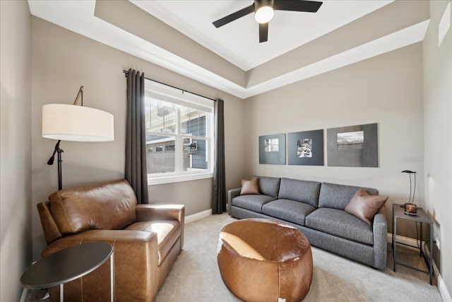 living room with ceiling fan, a raised ceiling, and light carpet