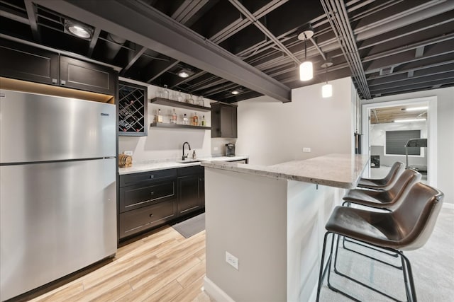 kitchen featuring light stone countertops, stainless steel fridge, light wood-type flooring, sink, and a breakfast bar area