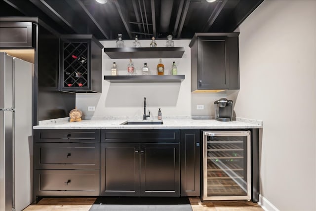 bar with light wood-type flooring, light stone counters, sink, wine cooler, and stainless steel refrigerator