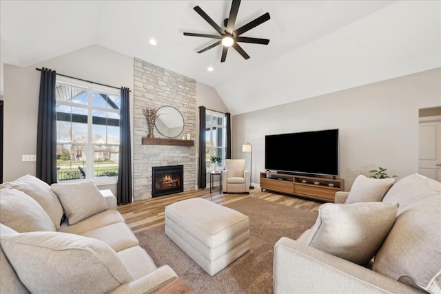 living room with hardwood / wood-style flooring, a stone fireplace, ceiling fan, and lofted ceiling