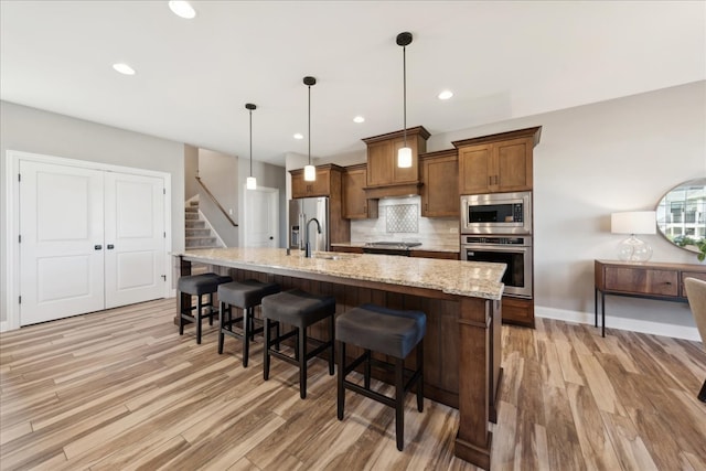 kitchen featuring decorative light fixtures, stainless steel appliances, light stone counters, and light hardwood / wood-style floors