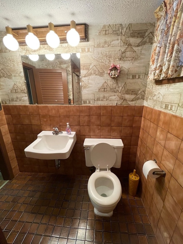 bathroom with a textured ceiling, toilet, tile walls, and sink