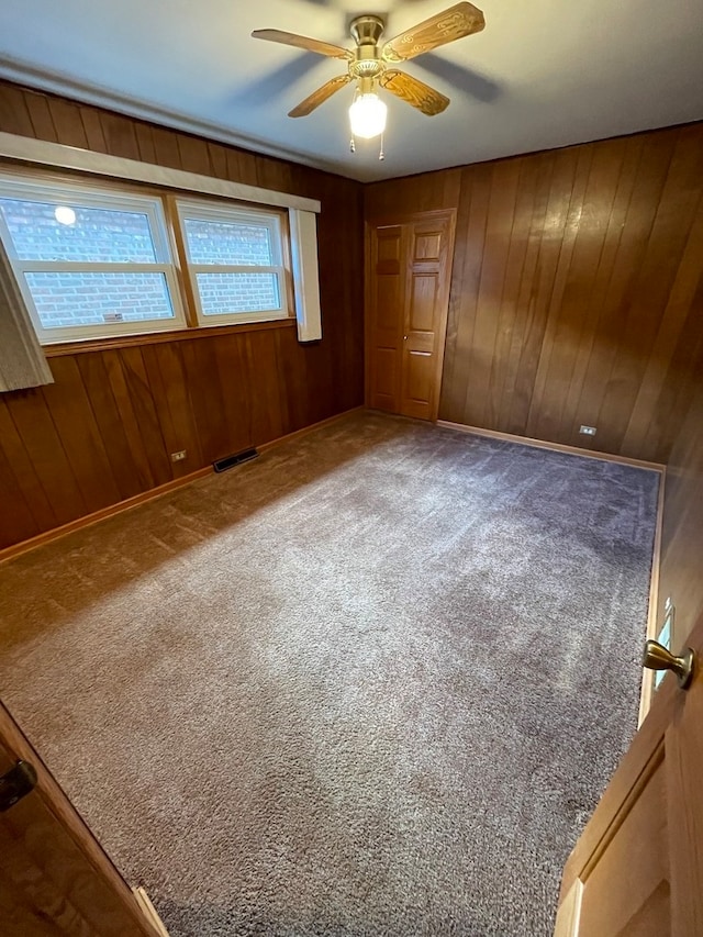 carpeted spare room with ceiling fan and wood walls