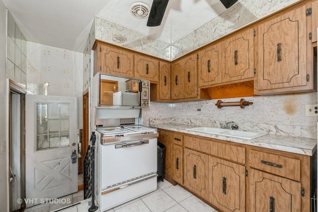 kitchen featuring backsplash, sink, ceiling fan, light tile patterned floors, and white range oven