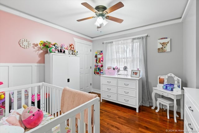 bedroom featuring a wainscoted wall, dark wood-type flooring, a ceiling fan, a nursery area, and a decorative wall