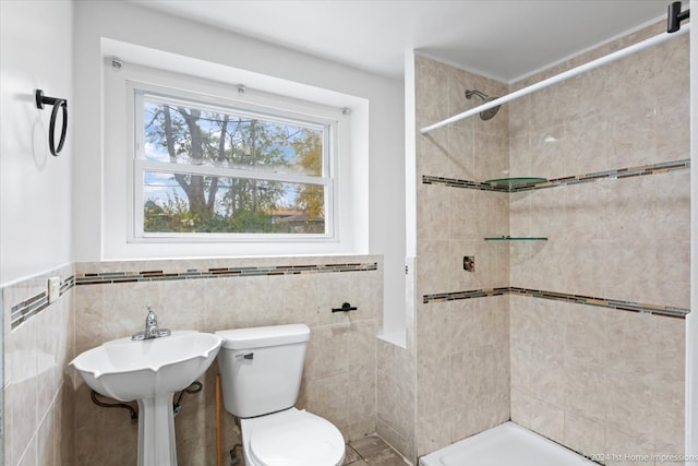 bathroom with tile walls, toilet, a tile shower, and wainscoting