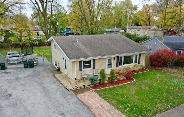 ranch-style house with aphalt driveway, roof with shingles, a front yard, and fence