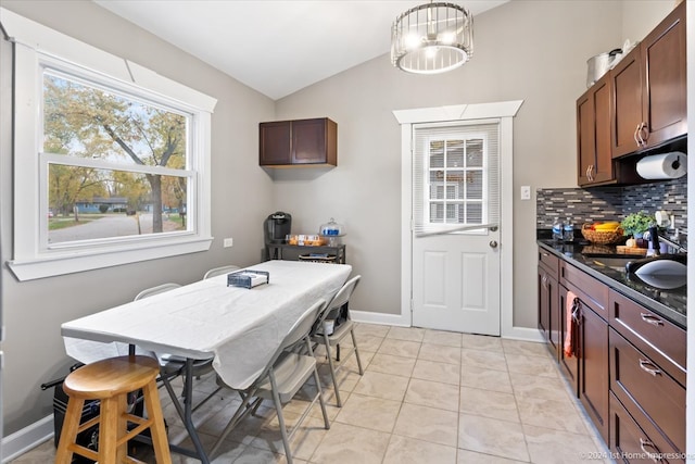 kitchen featuring baseboards, lofted ceiling, light tile patterned flooring, decorative backsplash, and a notable chandelier