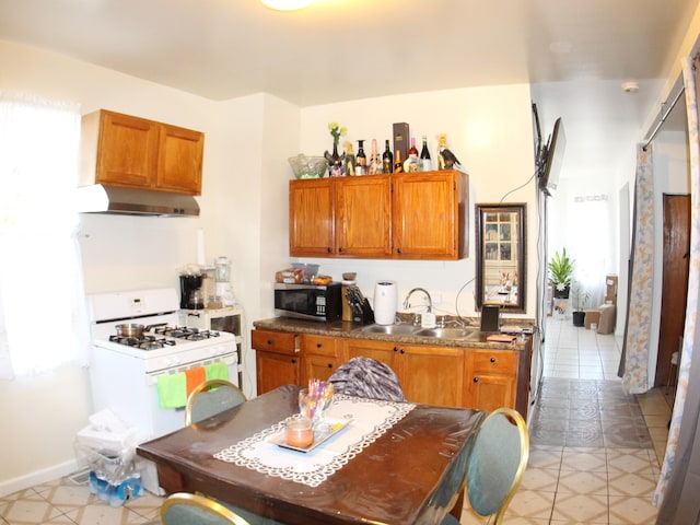 kitchen featuring white gas stove, sink, light tile patterned flooring, and plenty of natural light