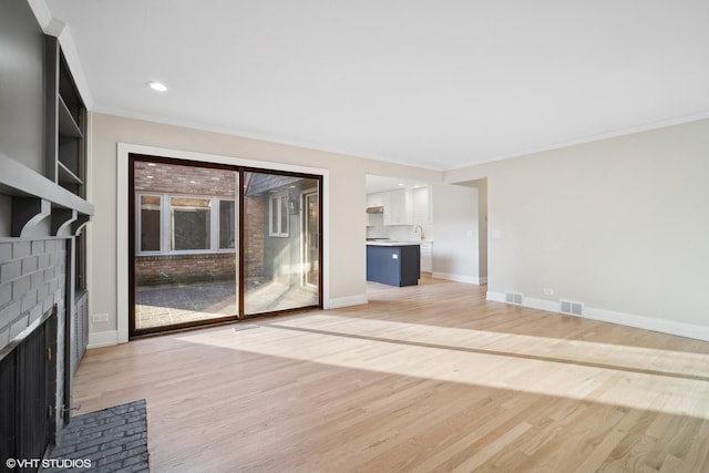 unfurnished living room featuring a brick fireplace, crown molding, and light hardwood / wood-style flooring