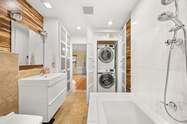 laundry area with stacked washer and dryer, tile walls, and sink