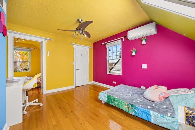 bedroom with a textured ceiling, a wall unit AC, ceiling fan, hardwood / wood-style floors, and lofted ceiling