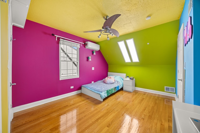 unfurnished bedroom with a wall mounted air conditioner, lofted ceiling with skylight, ceiling fan, a textured ceiling, and light hardwood / wood-style floors