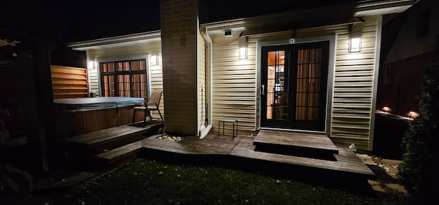 exterior entry at night featuring french doors, a hot tub, and a deck